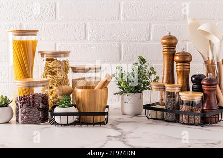 Stylish convenient storage of food and spices on the kitchen countertop with potted indoor plants. Beautiful kitchen background. Front view Stock Photo