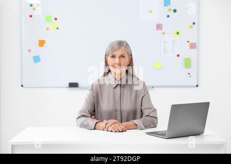 Professor sitting near laptop at desk in classroom Stock Photo