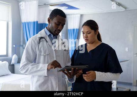 Diverse male and female doctors talking and using tablet in hospital room Stock Photo