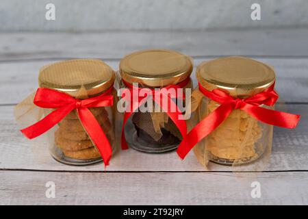 Three clear glass jars containing freshly baked cookies, placed in a line on a wooden table Stock Photo