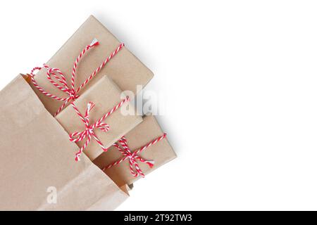 Christmas gift boxes wrapped in craft paper with striped red and white baker's twine in brown recycled paper bag isolated on white background with cop Stock Photo