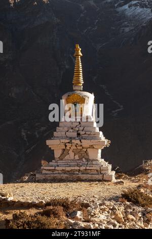 Buddhist stupa in Thame village with rocky mountain wall on the background, Sagarmatha National Park, Himalayas. Chorten damaged during earthquake in Stock Photo