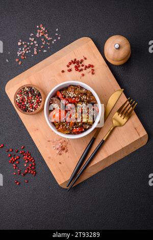 Warm salad with veal, tomatoes, peppers, zucchini, sesame, salt, spices and herbs on a dark concrete background Stock Photo