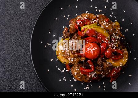 Warm salad with veal, tomatoes, peppers, zucchini, sesame, salt, spices and herbs on a dark concrete background Stock Photo