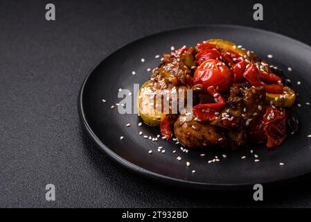 Warm salad with veal, tomatoes, peppers, zucchini, sesame, salt, spices and herbs on a dark concrete background Stock Photo