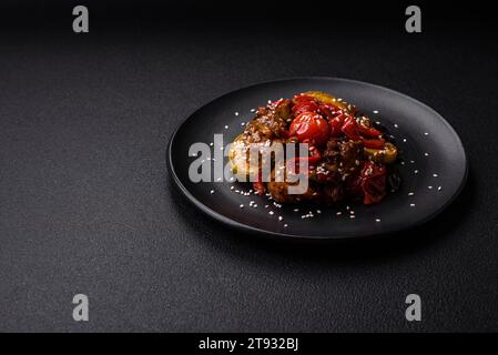 Warm salad with veal, tomatoes, peppers, zucchini, sesame, salt, spices and herbs on a dark concrete background Stock Photo