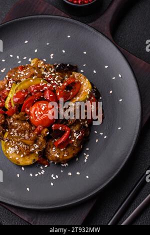 Warm salad with veal, tomatoes, peppers, zucchini, sesame, salt, spices and herbs on a dark concrete background Stock Photo