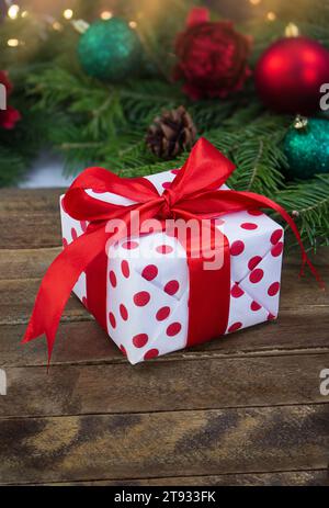 Gift box white red with polka dots on wooden boards with blurred toys. Christmas, New Year. Vertical. Copy space Stock Photo