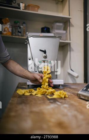 Hands of an unrecognizable person picking up fresh pasta as it comes out of the machine in a bakery Stock Photo