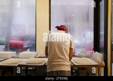 Unrecognizable baker dressed in white and wearing a red cap working on the doughs with his back to the camera on a table in a bakery Stock Photo