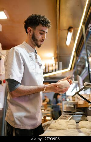 Young arabic pizza man in white apron kneading manually in the kitchen of a pizzeria Stock Photo
