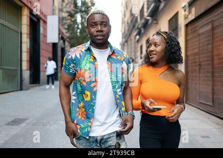 Young black couple in colorful and casual clothes talking while walking in the street on a sunny day Stock Photo