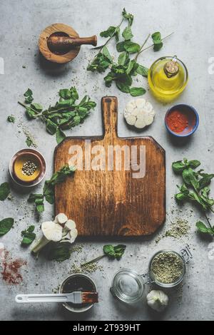Top view of empty wooden cutting board on grey concrete kitchen table with herbs ,spices, garlic,oil and mortar and pestle Stock Photo