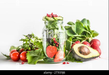 Green salad in jar with ingredients: green lettuce leaves, tomato, strawberry, avocado, cucumber and pomegranate seeds at white background. Healthy to Stock Photo