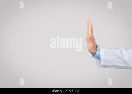 Male doctor in white coat with stop gesture, side view, grey background, free space Stock Photo