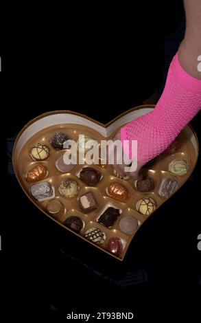 hand wearing pink fingerless glove taking a chocolate from a heart shaped box Stock Photo