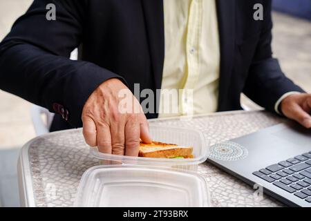 Close-up of an unrecognizable businessman eating a sandwich working on a terrace. Rest at work Stock Photo