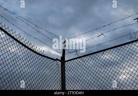 Close up photo of a barbed wire chain link fence against a dark stormy sky Stock Photo