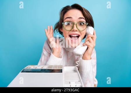 Portrait of astonished lady open mouth speak communicate cable telephone isolated on blue color background Stock Photo