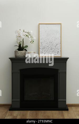 Picture frame, candles and orchid on fireplace near white wall indoors. Interior design Stock Photo