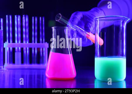 Scientist pouring luminous liquid into laboratory glassware at table, selective focus Stock Photo