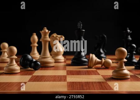 Many chess pieces on wooden checkerboard against black background, selective focus Stock Photo