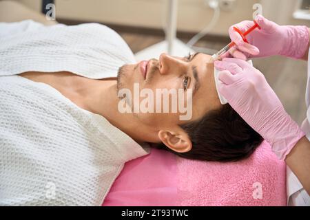 Doctor cosmetologist gives an injection to patient in frontal area Stock Photo