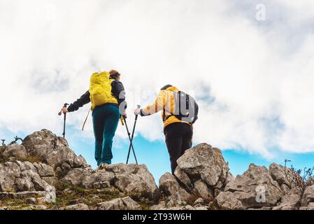 couple of mountaineers equipped with backpacks and trekking poles on top of a mountain. two people doing high mountain hiking. Stock Photo