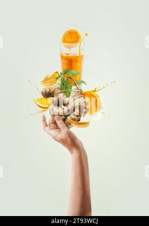 Women hand holding balancing ginger and orange immunity boosting drink with splashing and ingredients at light background. Creative healthy lifestyle. Stock Photo
