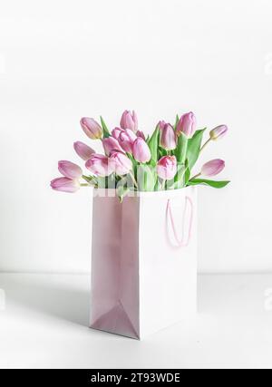Bunch of pink blooming tulips in gift box on table at white wall background. Celebrating in mothers day in springtime with beautiful flowers. Front vi Stock Photo