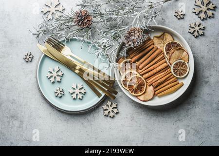 Christmas table setting with golden cutlery, pale blue plate, cinnamon sticks, dried orange natural dried apples and oranges and winter branches on gr Stock Photo