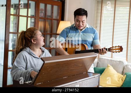 Young Asian chubby couple singing and playing acoustic guitar and piano together. Man and woman enjoying musical instrument. People in a band practicing in the house Stock Photo