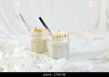 Chia seeds from the Salvia hispanica plant. Glass cup containing the seeds hydrated with natural yogurt, oat flakes, linseed seeds and on top banana, Stock Photo