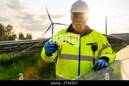 Senior engineer holding a wind turbine model at a solar photovoltaic panel system at sunset. Alternative energy ecological concept. Stock Photo