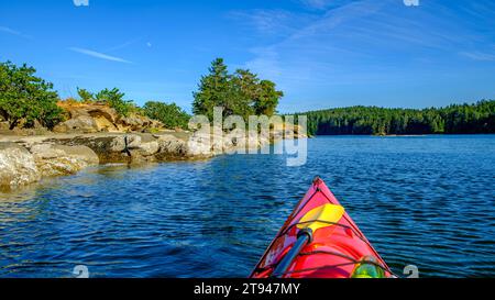 The bow of a red kayak in the water near the shore of a small uninhabited island in the Salish Sea. Stock Photo