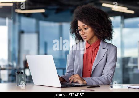 A young African-American businesswoman is sitting at a desk in the office and is concentrating on working on a laptop. Stock Photo