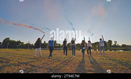 A group of friends spraying multi-colored smoke at sunset. Stock Photo