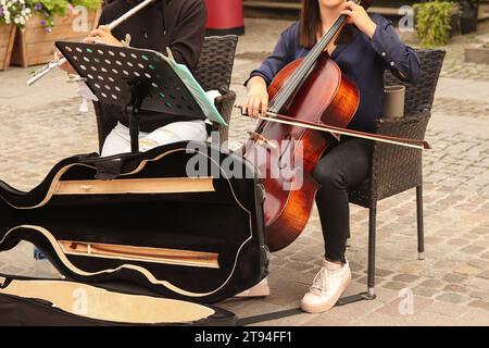 Street music band performing on old city background. Close up women playing flute and double bass, singing song to raise money in hat. Gdansk Stock Photo