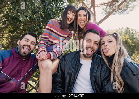 Joyful group of young friends sharing a laugh while sitting in a city park, embodying the spirit of youth and friendship Stock Photo
