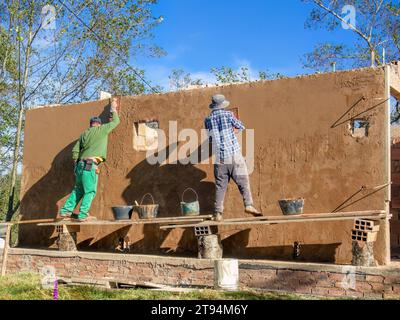 Two workers plastering a wall standing in a very rustic and unstable scaffolding,  at a construction site near the town of Arcabuco, in central Colomb Stock Photo