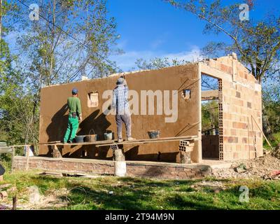 Two workers plastering a wall standing in a very rustic and unstable scaffolding,  at a construction site near the town of Arcabuco, in central Colomb Stock Photo