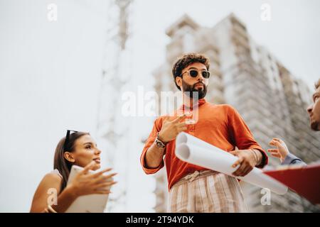 Architects and engineers discuss project details on a construction site. Teamwork ensures sustainable, industrial design for urban development. Stock Photo