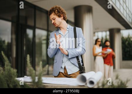 Diverse architects and engineers collaborate outdoors, discussing an architectural blueprint. Stock Photo