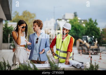 Diverse group of architects and engineers collaborating outdoors, discussing and developing a construction project with innovation and teamwork. Stock Photo