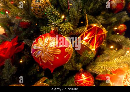 Red and gold Christmas ball bauble ornament with glitter details against out of focus Christmas tree warm green background Stock Photo