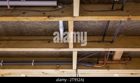 Under floor view showing various pipes and cables in a wooden beam construction with insulation material Stock Photo