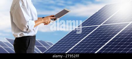 Female person wearing formal outfit controls the solar energy station remotely using a digital tablet. Stock Photo