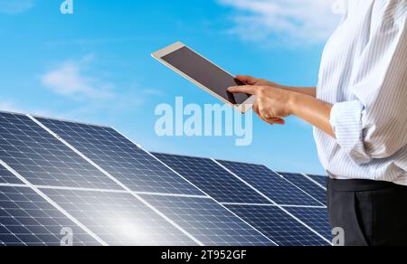 Female person wearing formal outfit controls the solar energy station remotely using a digital tablet. Stock Photo