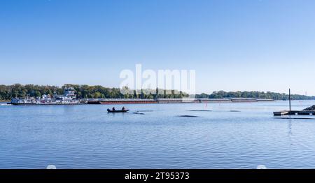 Hannibal, MO - 20 October 2023: Large tug boat pushing rows of barges with grain down the Upper Mississippi river past fishermen Stock Photo