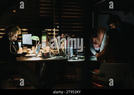 Diverse professionals collaborating late at night, analyzing data and discussing strategies for project deadline and business growth. Stock Photo